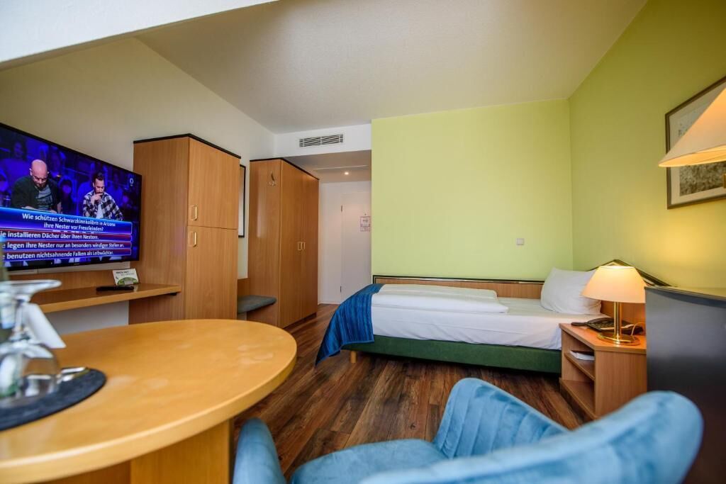 A hotel room with a bed, a TV, a desk, and a chair.
