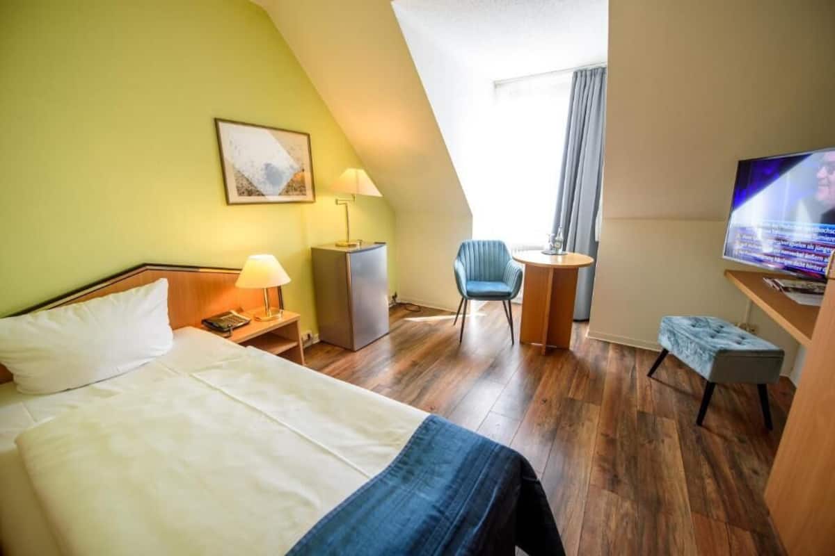 A hotel room with a bed, a desk with a TV, a chair, and a small table.