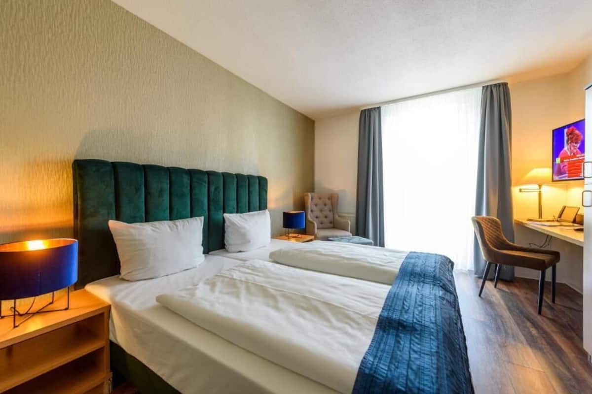 A hotel room with two beds, a desk, a chair, and a TV.