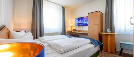 Quarto de hotel com uma cama, uma escrivaninha, uma televisão e uma mesinha.