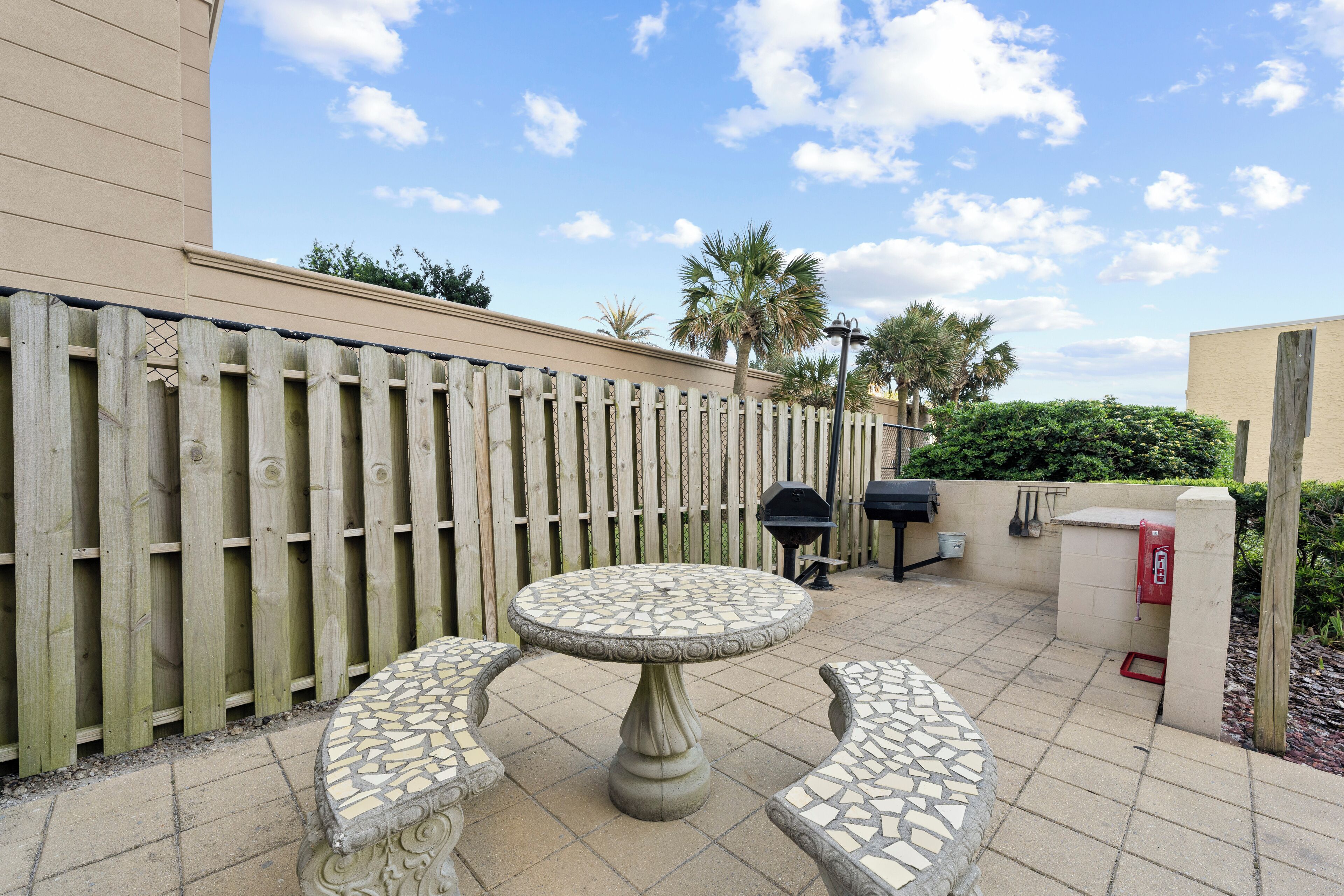 Une terrasse avec une table et des bancs en mosaïque, une clôture en bois et un barbecue.