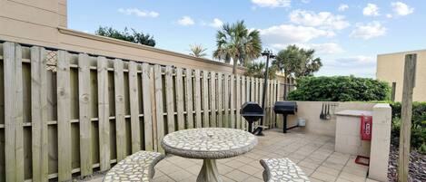 A patio with a mosaic table and benches, a wooden fence, and a barbecue grill.