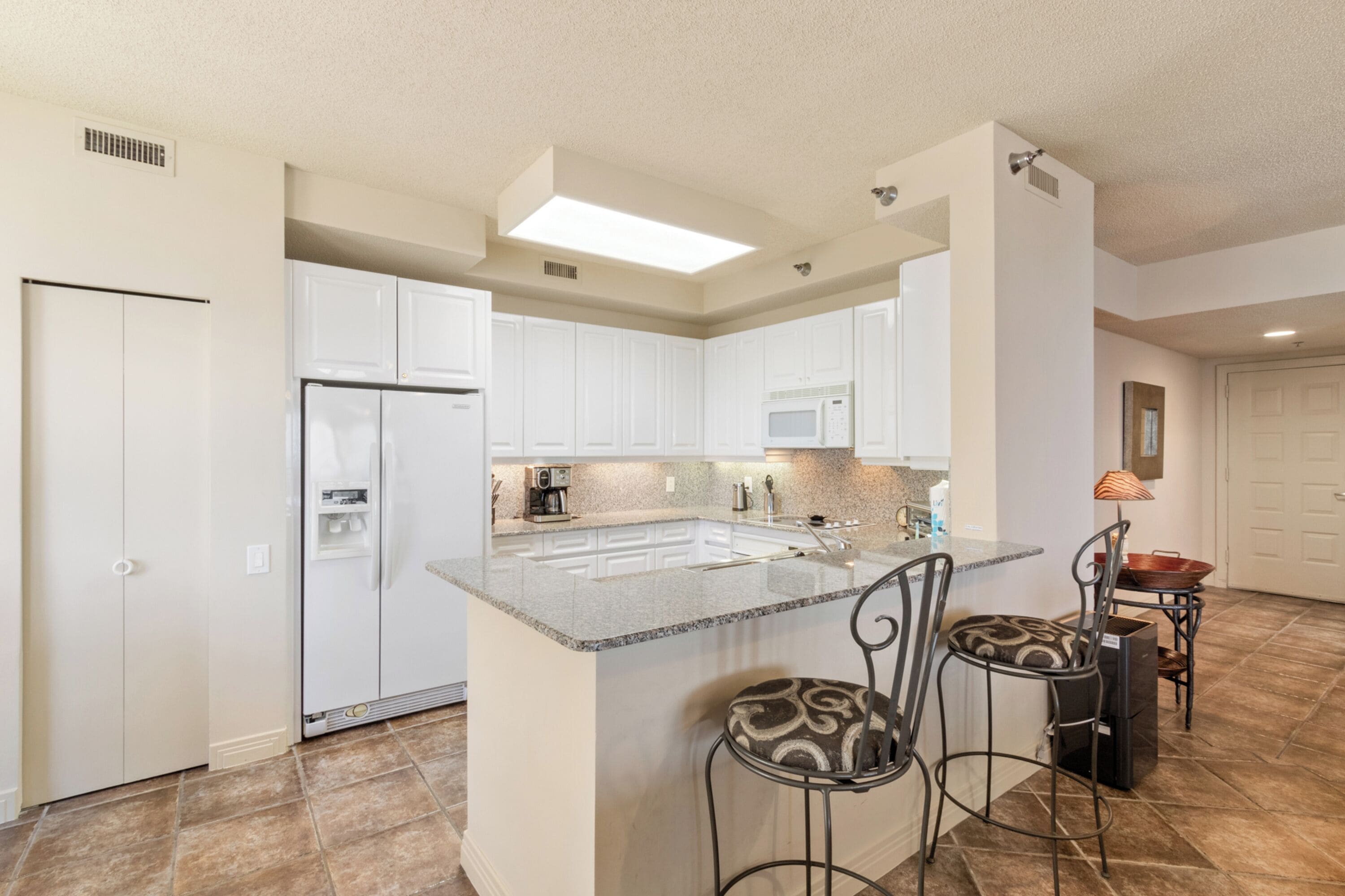 A modern kitchen with white cabinets, a large island with bar stools, a microwave, and a refrigerator.