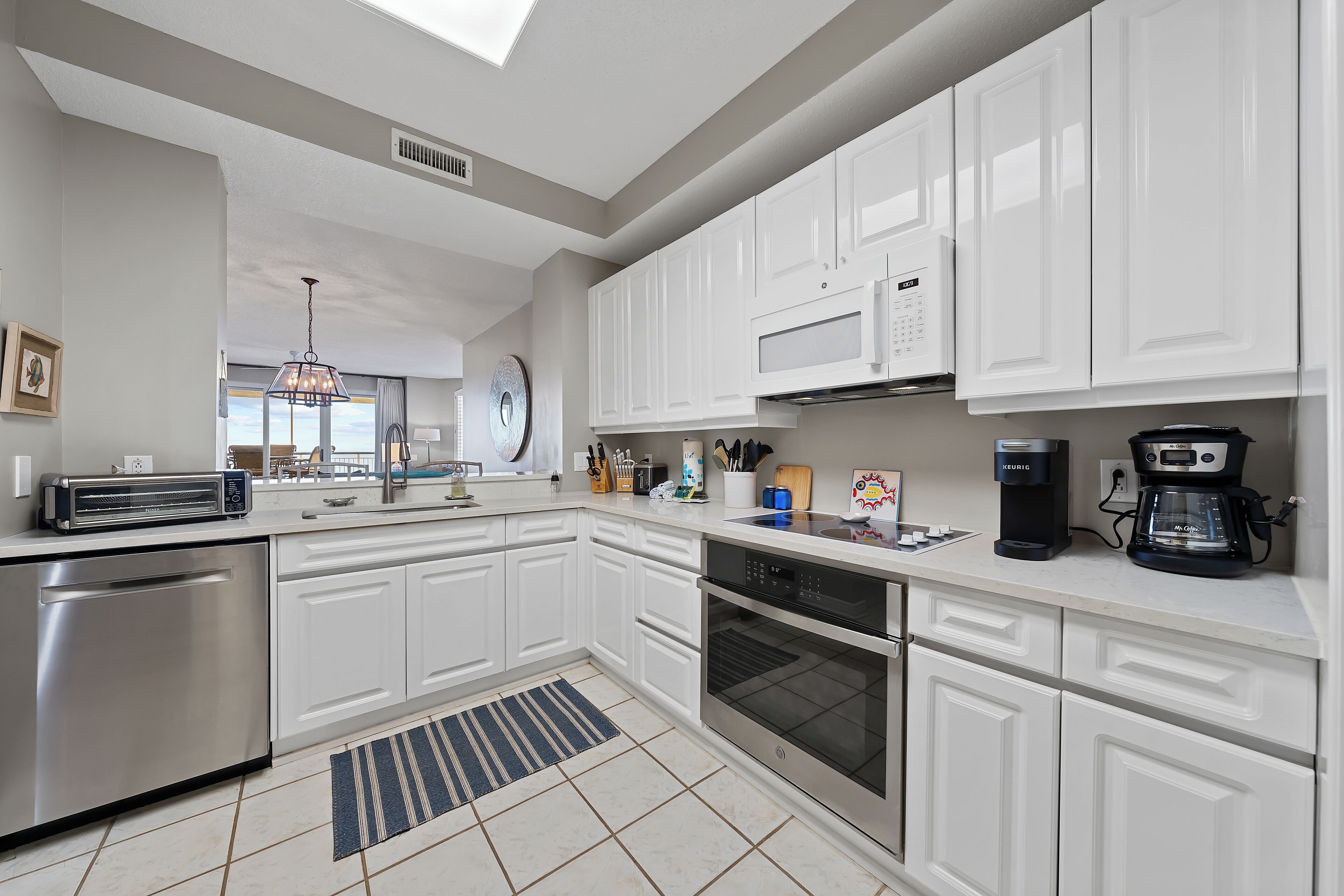 A modern kitchen with white cabinets, stainless steel appliances, and a large window.