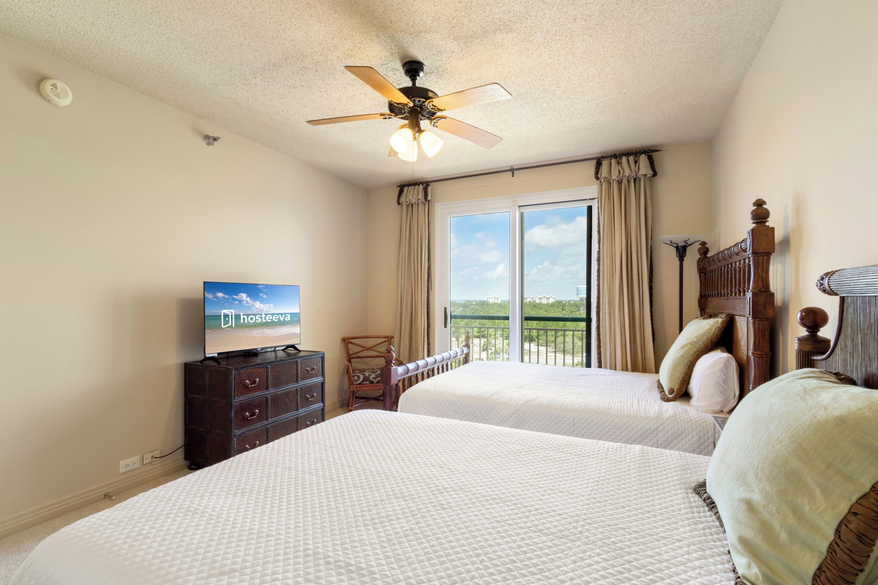 A hotel room with two beds, a ceiling fan, a television, and a view of the outdoors.