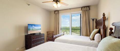 A hotel room with two beds, a ceiling fan, a television, and a view of the outdoors.