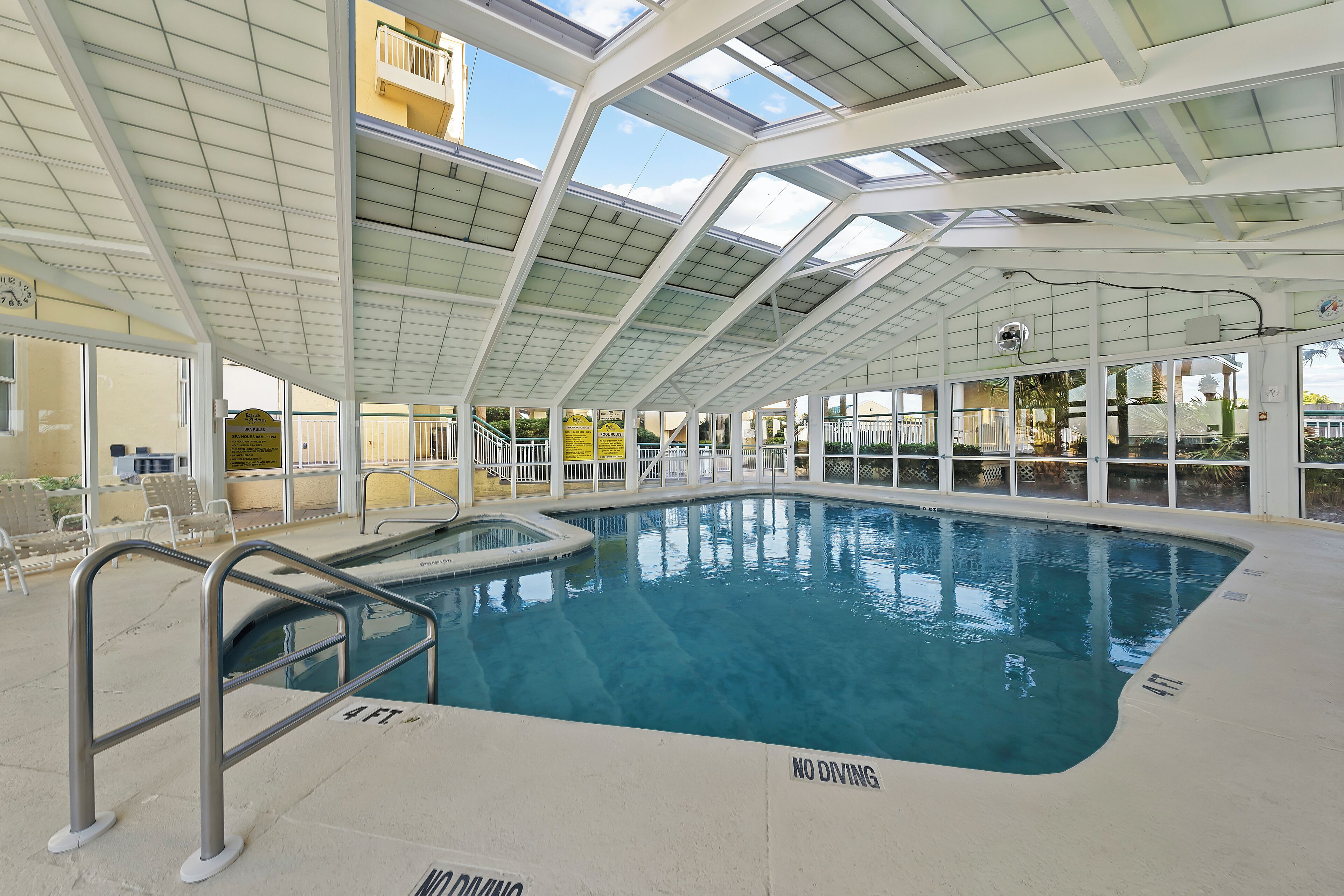 An indoor swimming pool with a glass ceiling, a no diving sign, and a lifeguard chair.