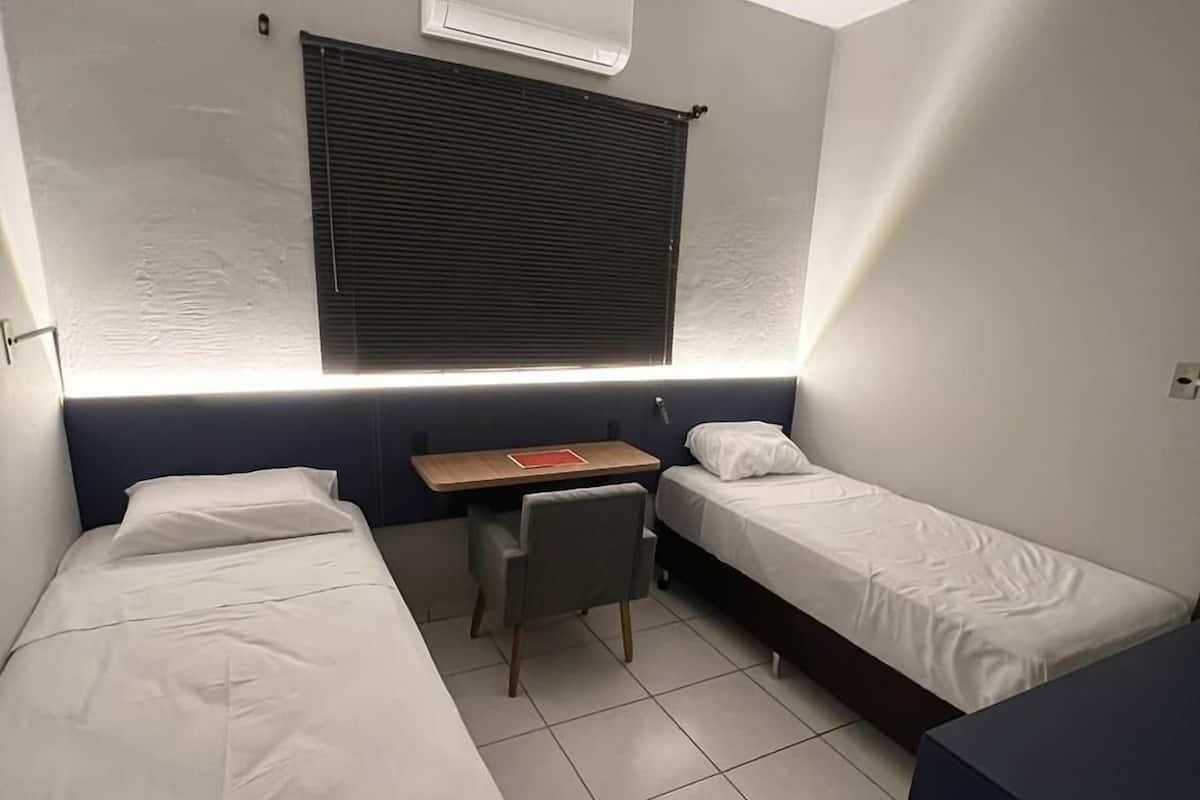 Ein kleines, modernes Zimmer mit zwei Einzelbetten, einem Schreibtisch und einem Stuhl.