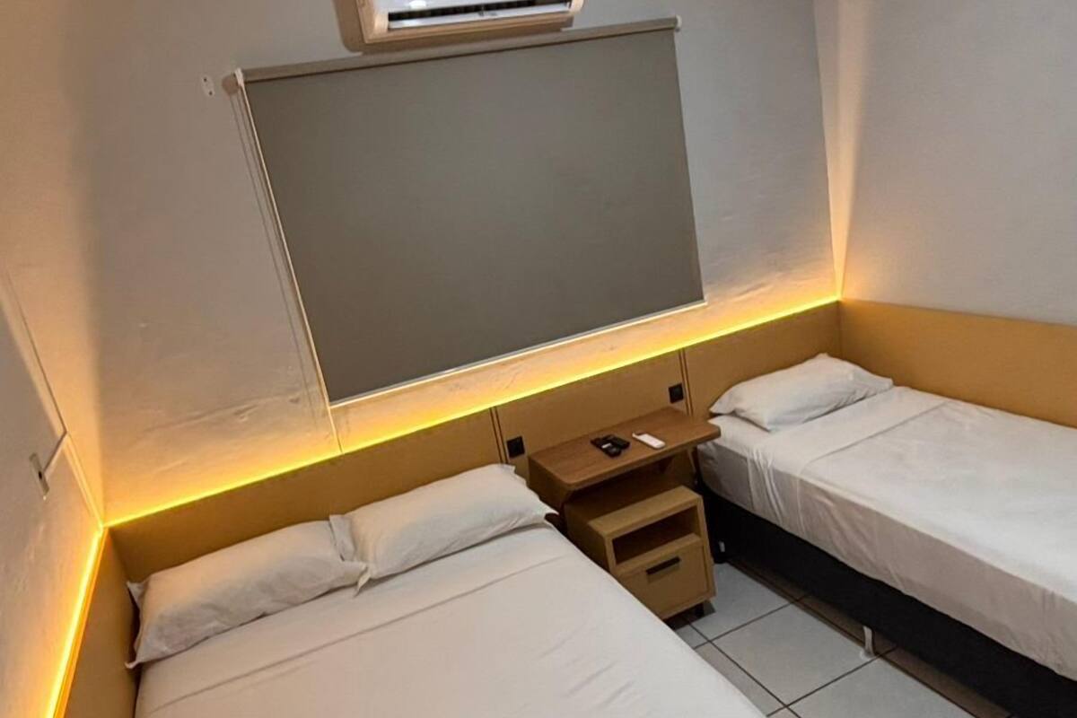 Ein Hotelzimmer mit zwei Einzelbetten, einer Decken-Klimaanlage und einem Nachttisch mit Lampe.