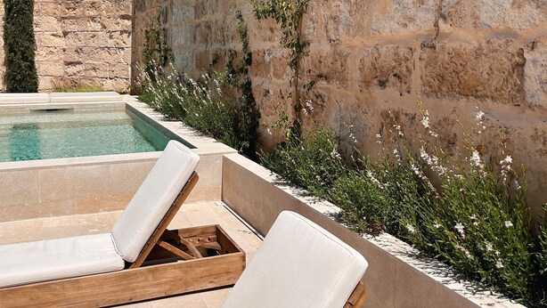 Zona de piscina con sillas de descanso y un muro de piedra.