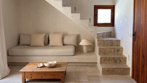Una escalera con una puerta de madera, un sofá color beige con cojines y una mesita baja con cuencos.