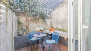 Eine kleine Terrasse mit einem runden Tisch und blauen Stühlen, einer Obstschale und einem Blumentopf.