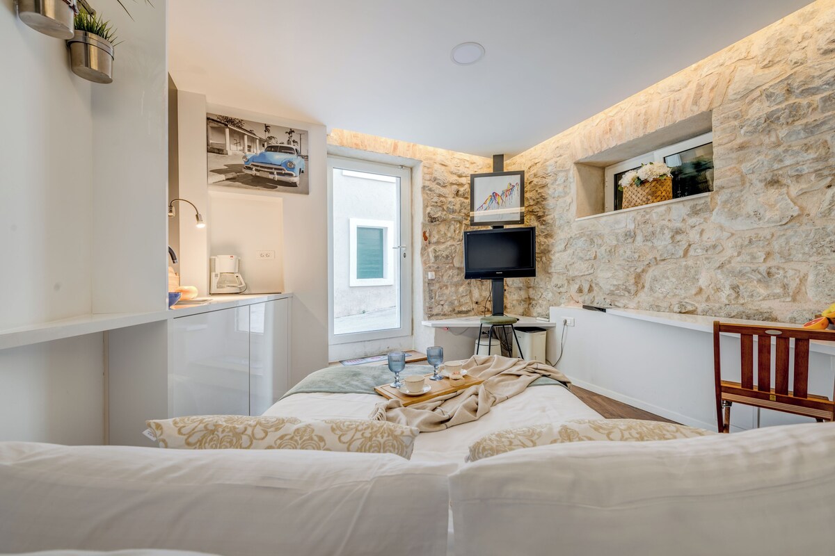 Un dormitorio con pared de piedra, una cama con ropa de cama estampada, un televisor y una mesita con una bandeja.