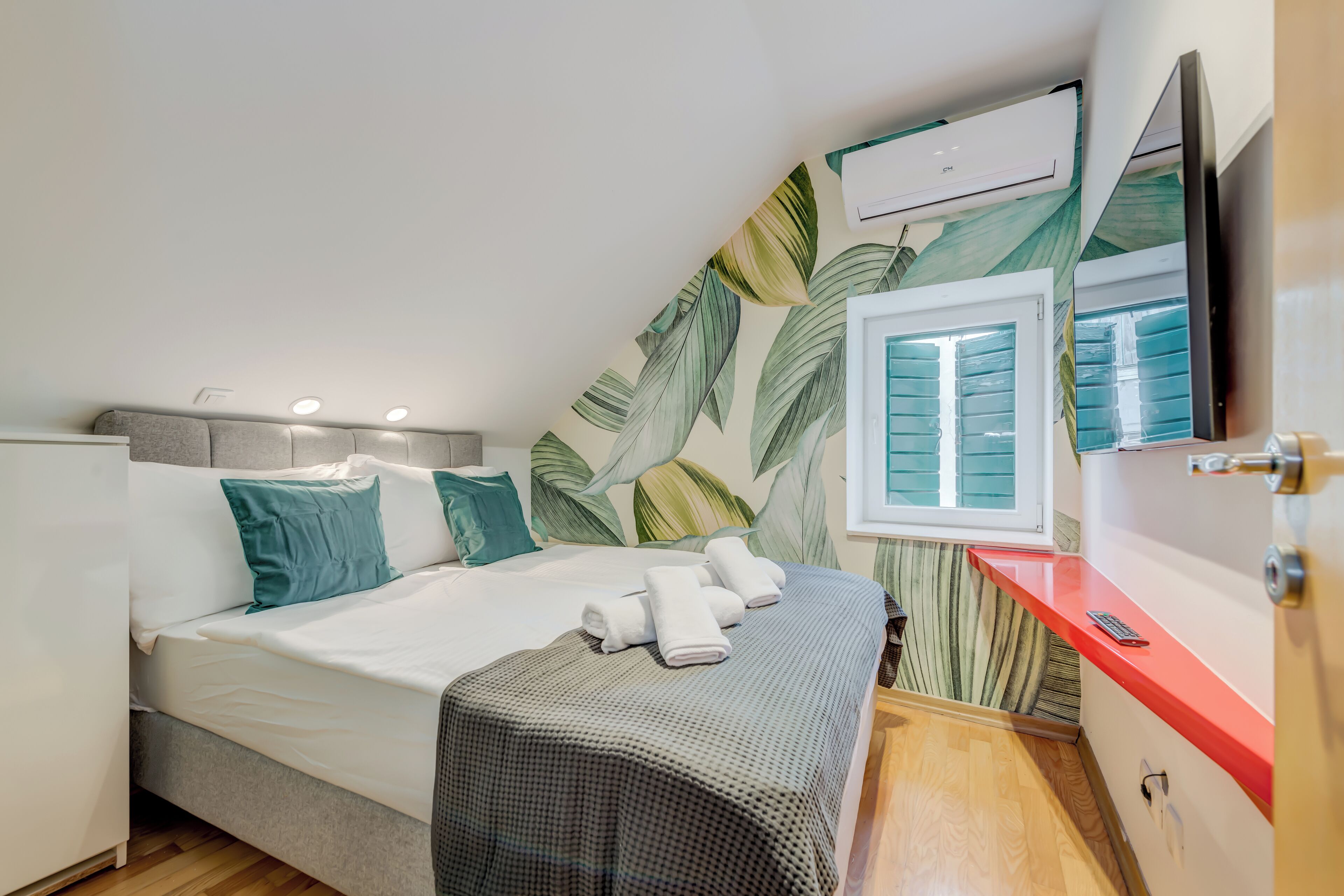 A bedroom with a bed, pillows, a blanket, a TV, and an air conditioning unit.
