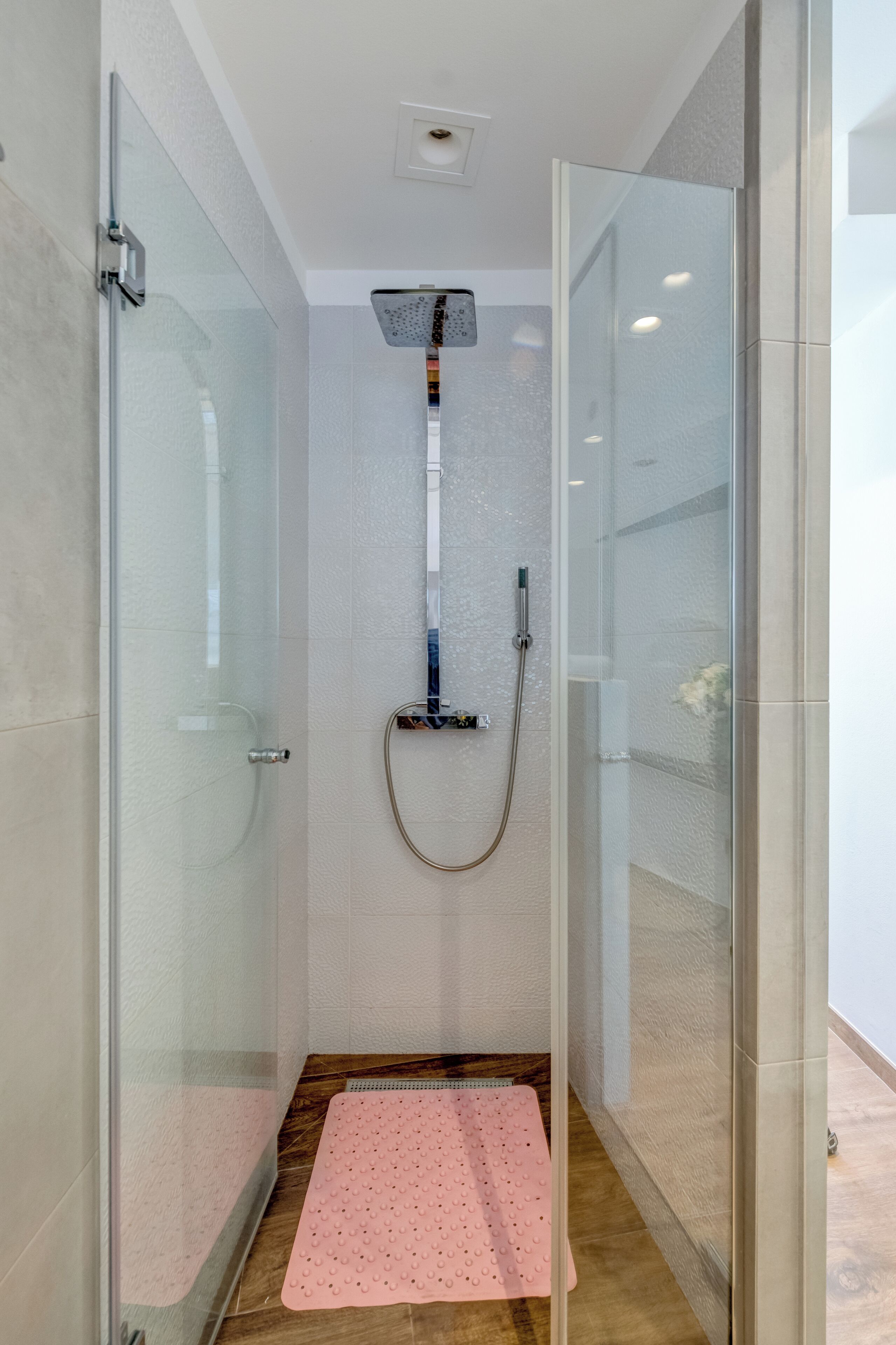 A glass-enclosed shower with a handheld showerhead and a handheld shower attachment.