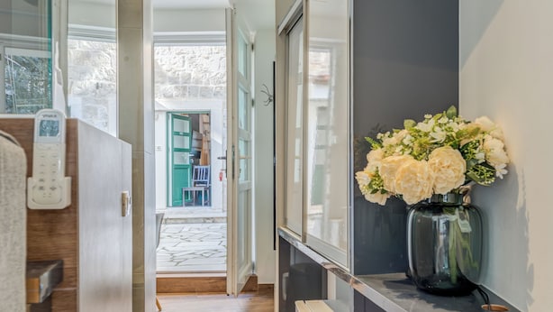 Ein Flur mit Holzboden, einer weißen Wand mit schwarzem Regal, einer Vase mit weißen Blumen und einer Tür, die in einen Raum mit grüner Tür führt.