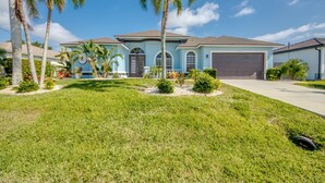 A two-story house with a light blue exterior, a garage, and a well-maintained lawn with palm trees. - Cape Coral Luxury Waterfront- Direct Gulf Access- Htd Pool- Bikes-5BDR -Villa 12 (Cape Coral)