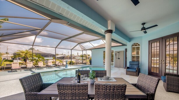 A covered outdoor area with a pool, lounge chairs, and a table with chairs. - Cape Coral Luxury Waterfront- Direct Gulf Access- Htd Pool- Bikes-5BDR -Villa 12 (Cape Coral)