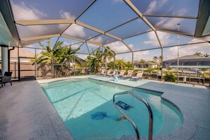 A swimming pool with a clear blue water, surrounded by lounge chairs and palm trees.