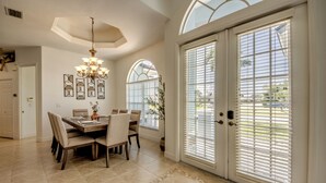 A dining area with a table set for four, a chandelier, and a large window with blinds. - Cape Coral Luxury Waterfront- Direct Gulf Access- Htd Pool- Bikes-5BDR -Villa 12 (Cape Coral)