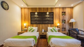 Habitación de hotel con dos camas, cabecero de madera, lámparas de noche, un escritorio y una silla.