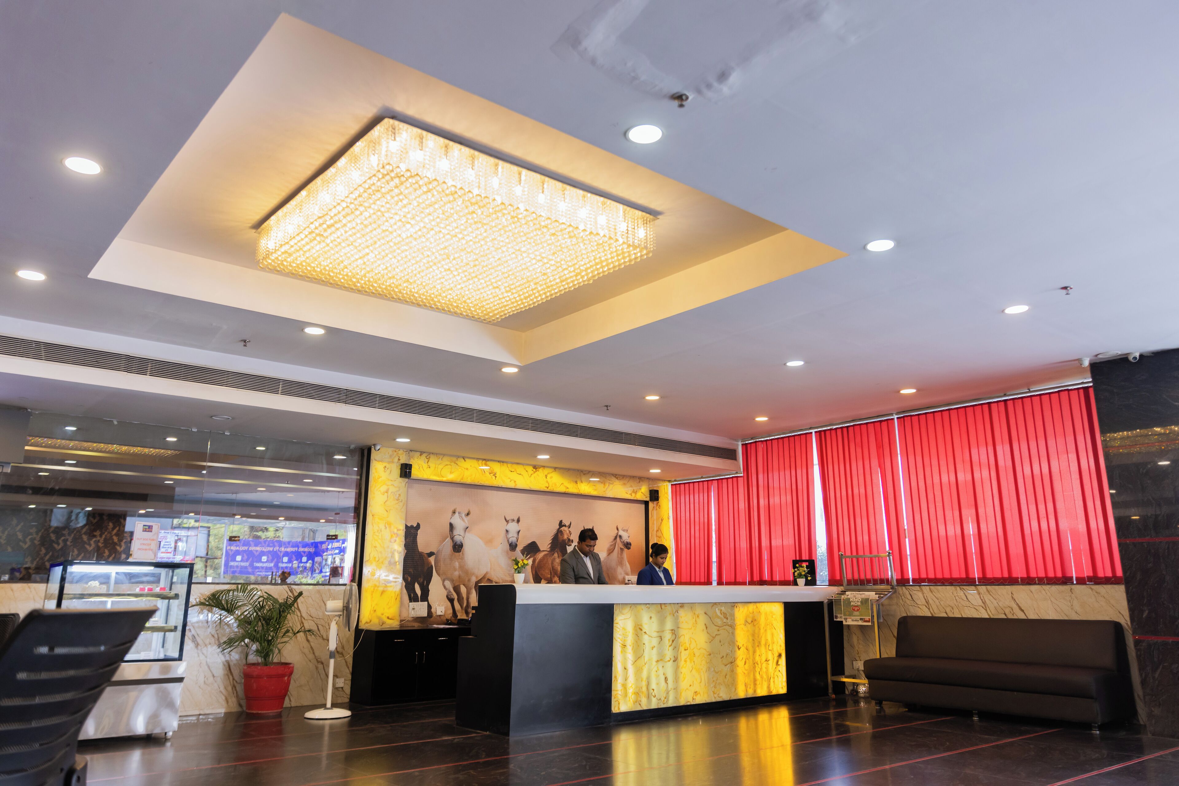 Un hall d'accueil d'hôtel avec un lustre moderne, un rideau rouge et un comptoir de réception.
