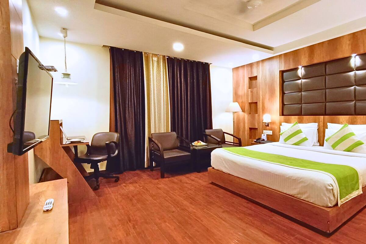 A hotel room with a large bed, a desk with a chair, a TV, and a wooden headboard.