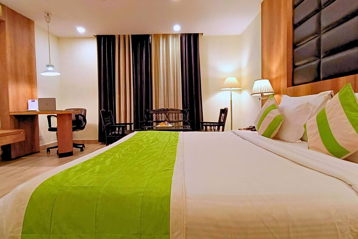 A hotel room with a large bed, a desk, a chair, and a lamp.