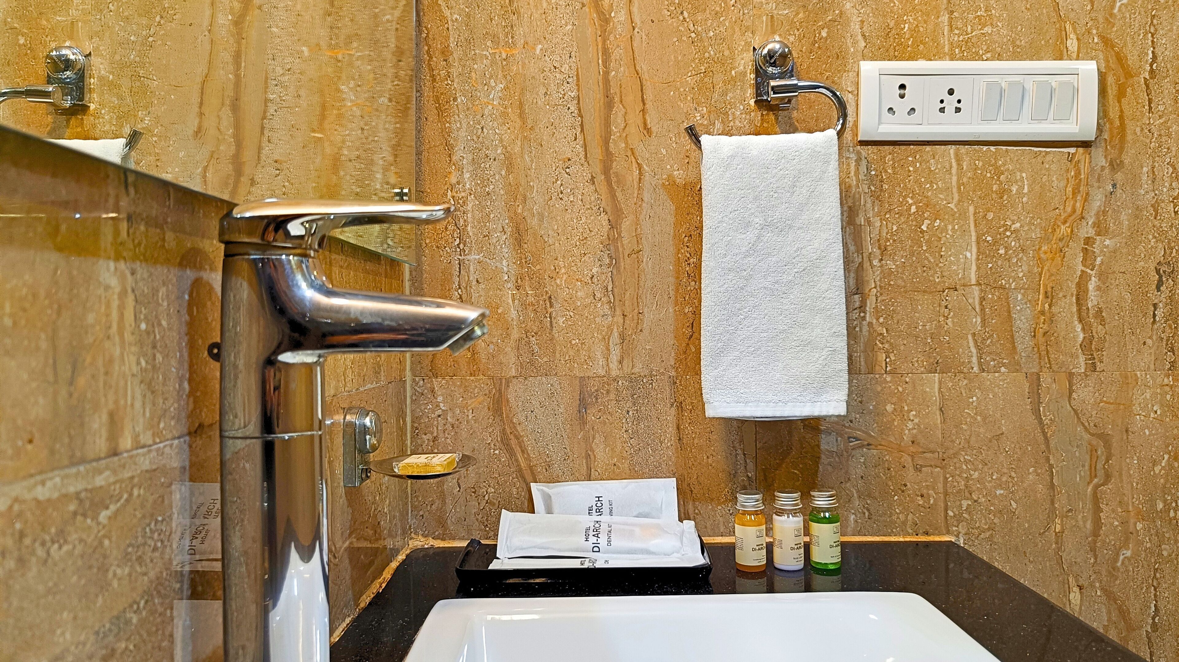 A bathroom with a marble wall, a sink, a towel rack, and toiletries.