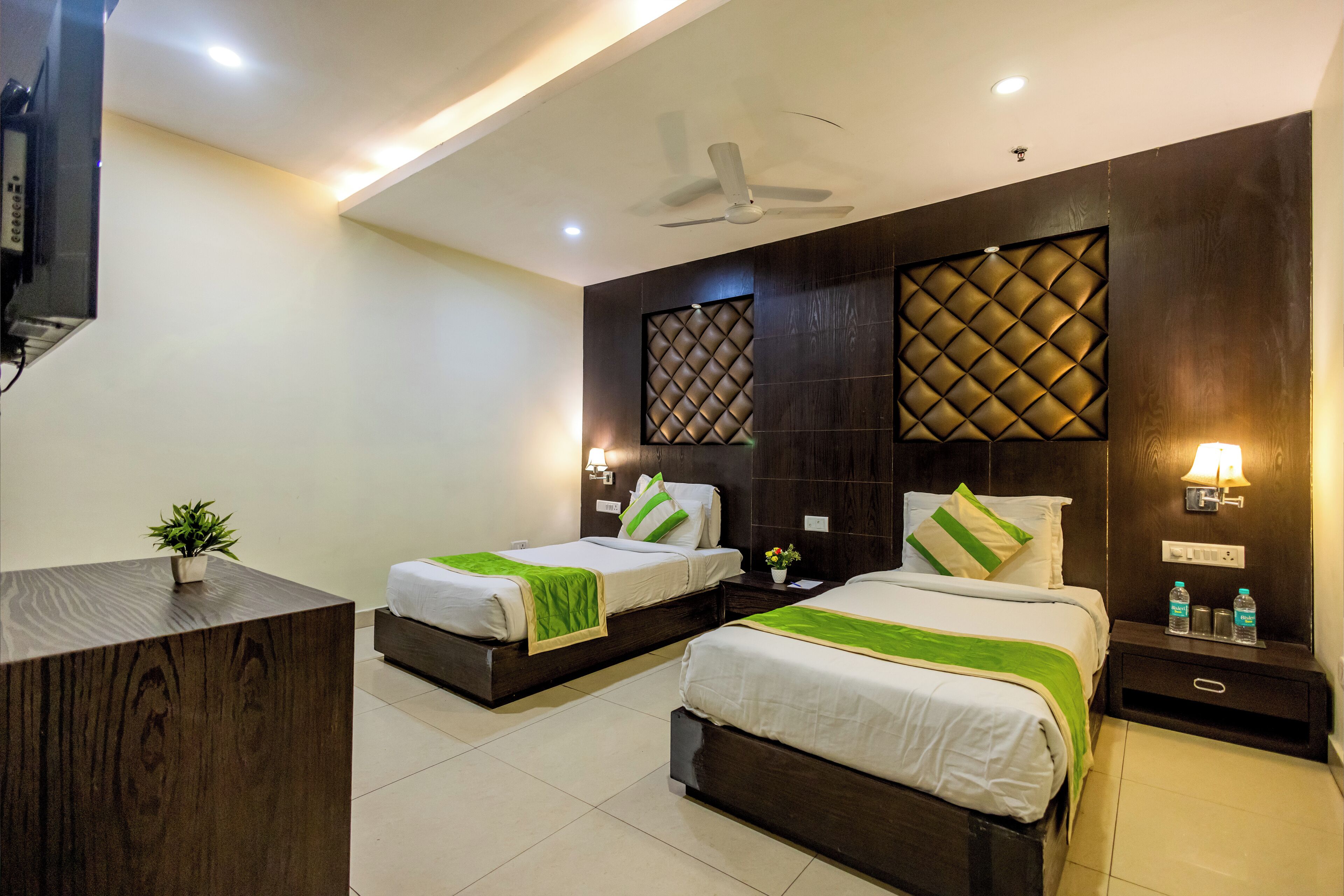 A hotel room with two beds, a desk, a ceiling fan, and a TV.