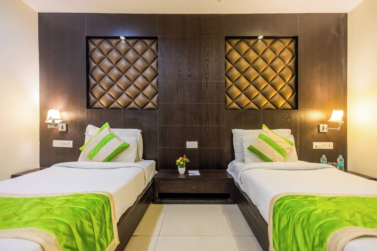 A hotel room with two beds, a nightstand, and a wall-mounted light fixture.