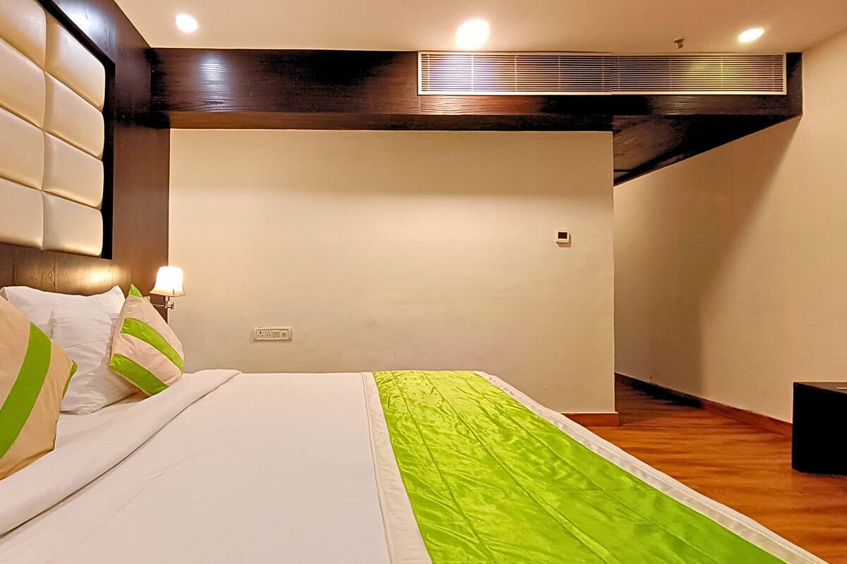 A hotel room with a large bed, a headboard, a bedside lamp, and a wall-mounted air conditioning unit.