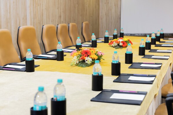 A conference room with a long table, chairs, water bottles, and flower centerpieces. - Hotel Di Arch Lucknow (Lucknow)