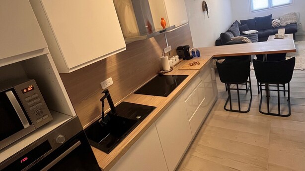 A modern kitchen with a built-in oven, microwave, and sink. There is a dining area with a table and chairs.