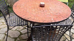 A round outdoor table with a mosaic tile top, surrounded by metal chairs.