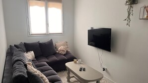 A living room with a dark sofa, a small table, a TV, and a window with blinds.