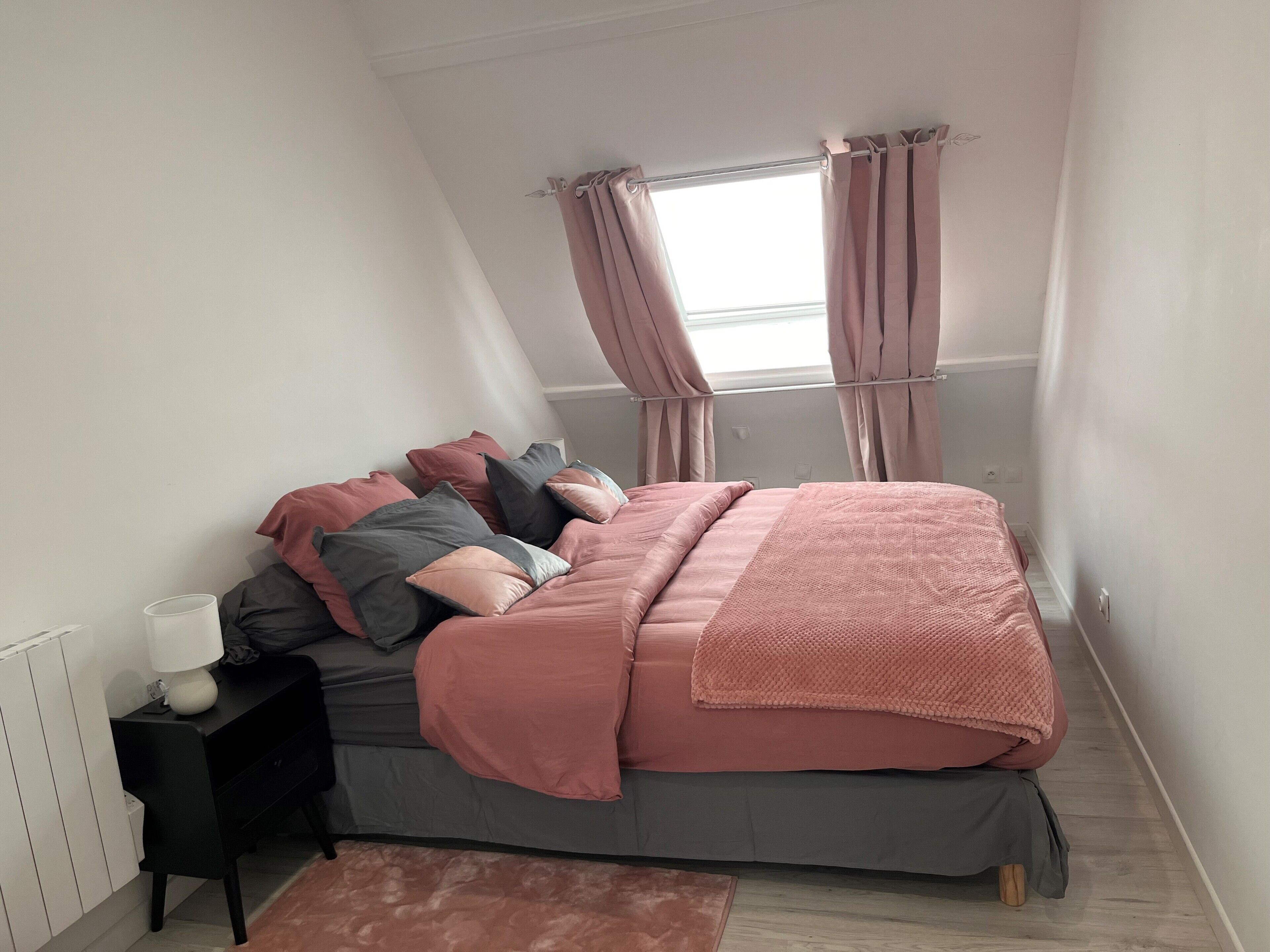 Une chambre à coucher avec un lit, une table de chevet, une lampe et une fenêtre avec des rideaux.