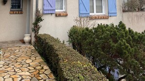A house with a tiled roof, a stone-paved entrance, and a small garden area.