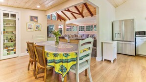 Comedor con una mesa redonda, sillas y mantel estampado. Se observa una zona de cocina con refrigerador y armarios.