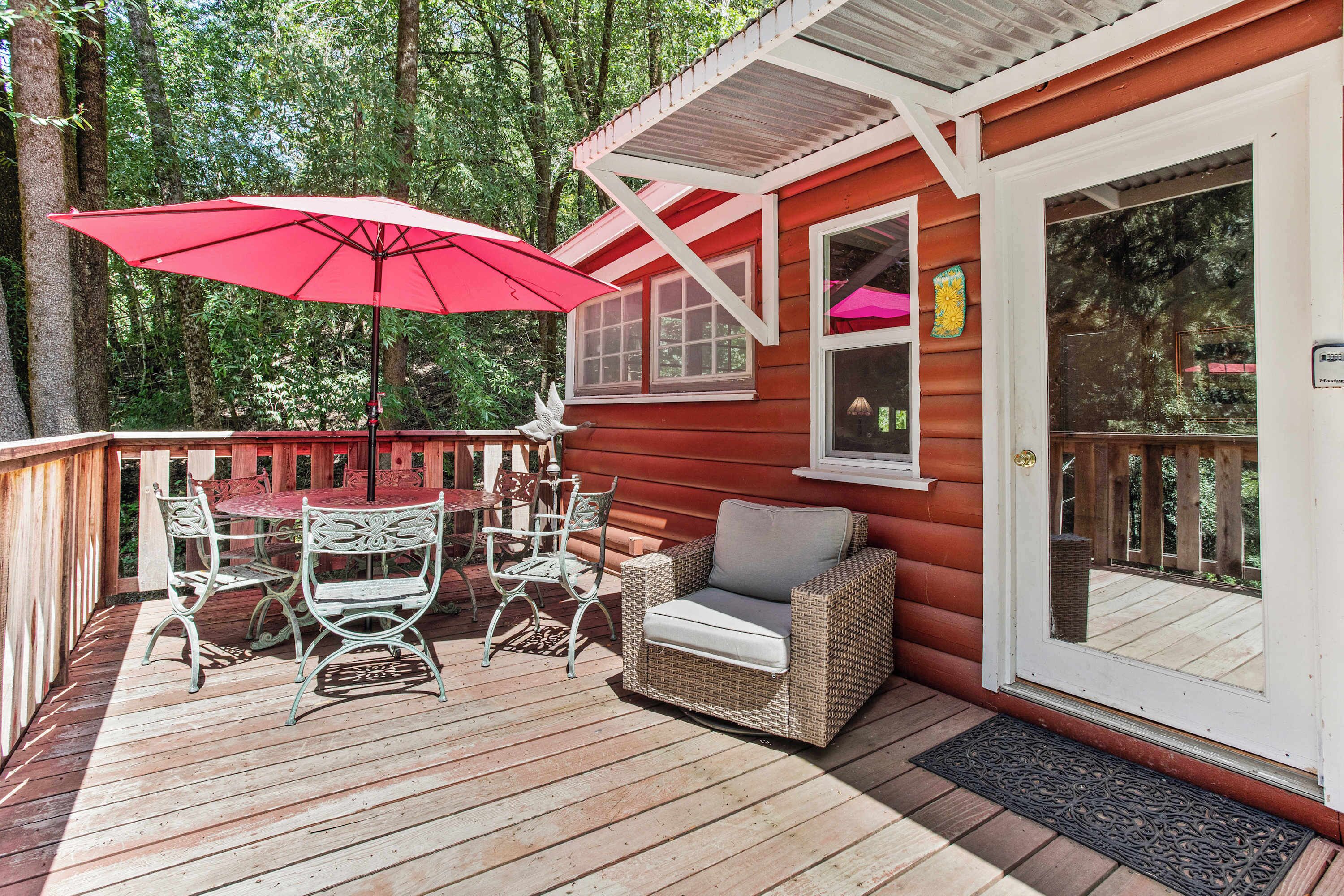 A wooden deck with a red umbrella, wicker furniture, and a glass door.