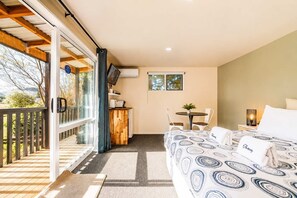 Ein Schlafzimmer mit einem Bett, einem kleinen Tisch mit Stühlen, einem Fernseher und einem Balkon mit Geländer.