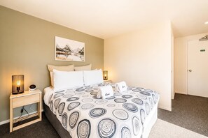 A hotel room with a bed, a nightstand, a lamp, a painting, and a door.