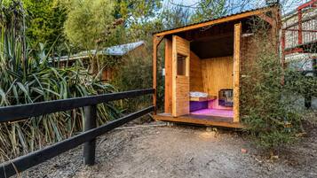 A small wooden cabin with a single bed, a table, and a bench.