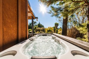 Ein Whirlpool mit einer Holzterrasse und Blick auf einen angelegten Garten mit Bäumen und Sträuchern.