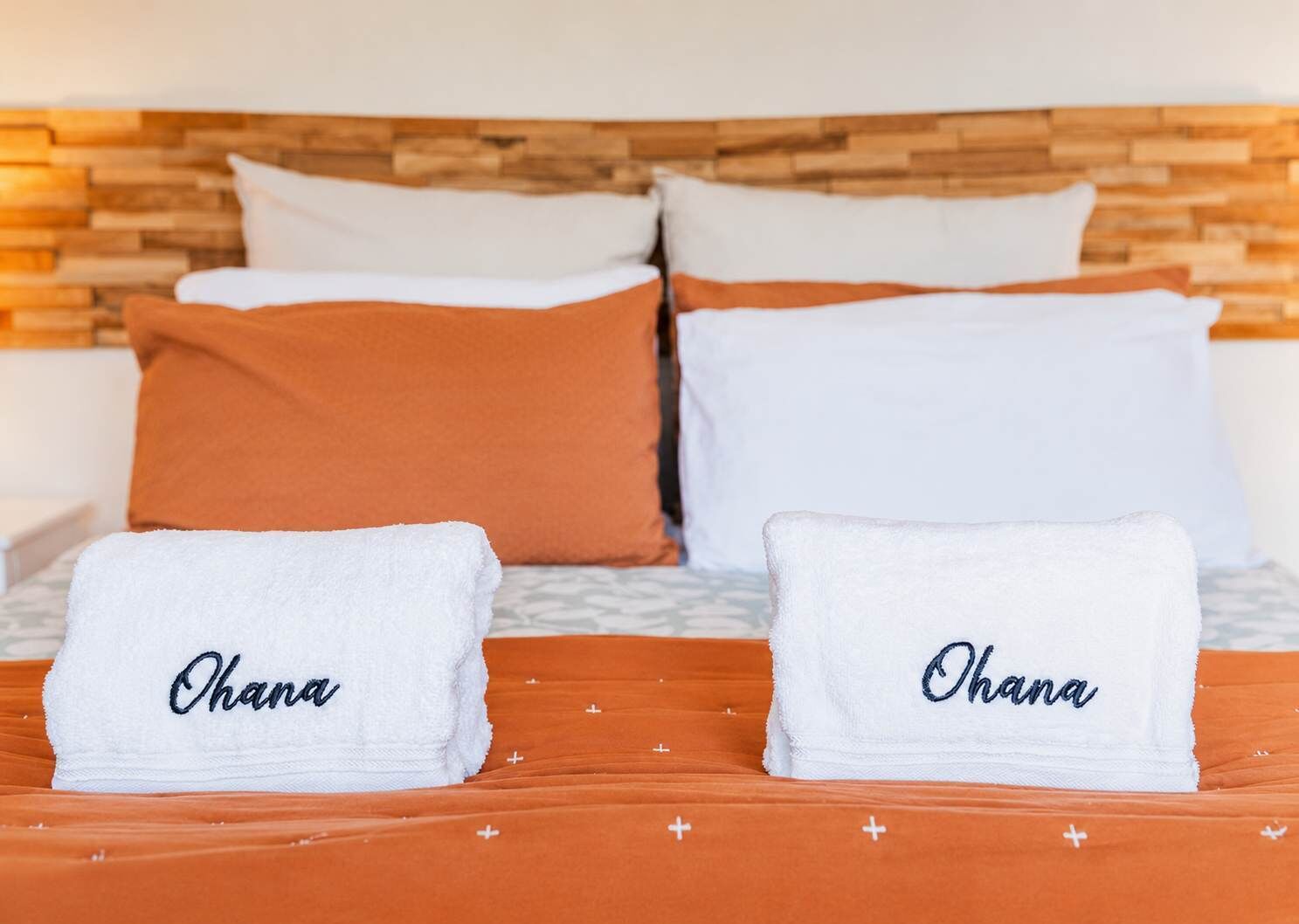 Un lit sur lequel sont posées deux serviettes blanches, chacune ornée du nom « Ohana » brodé dessus.