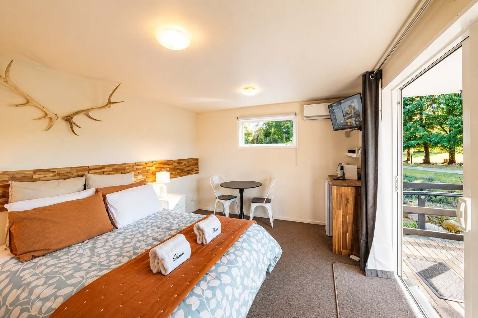 A hotel room with a bed, a desk, a chair, a television, and a large window with a view of trees.
