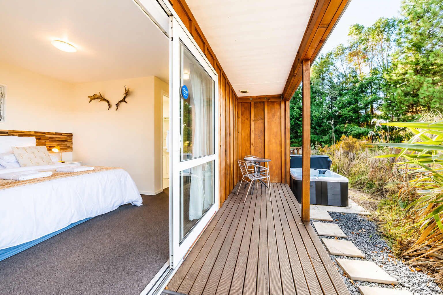 A hotel room with a bed, a desk, and a sliding glass door leading to an outdoor deck.