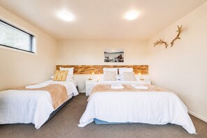 Habitación de hotel con dos camas, cabecera de madera, mesita de noche con lámpara y un cuadro colgado en la pared.