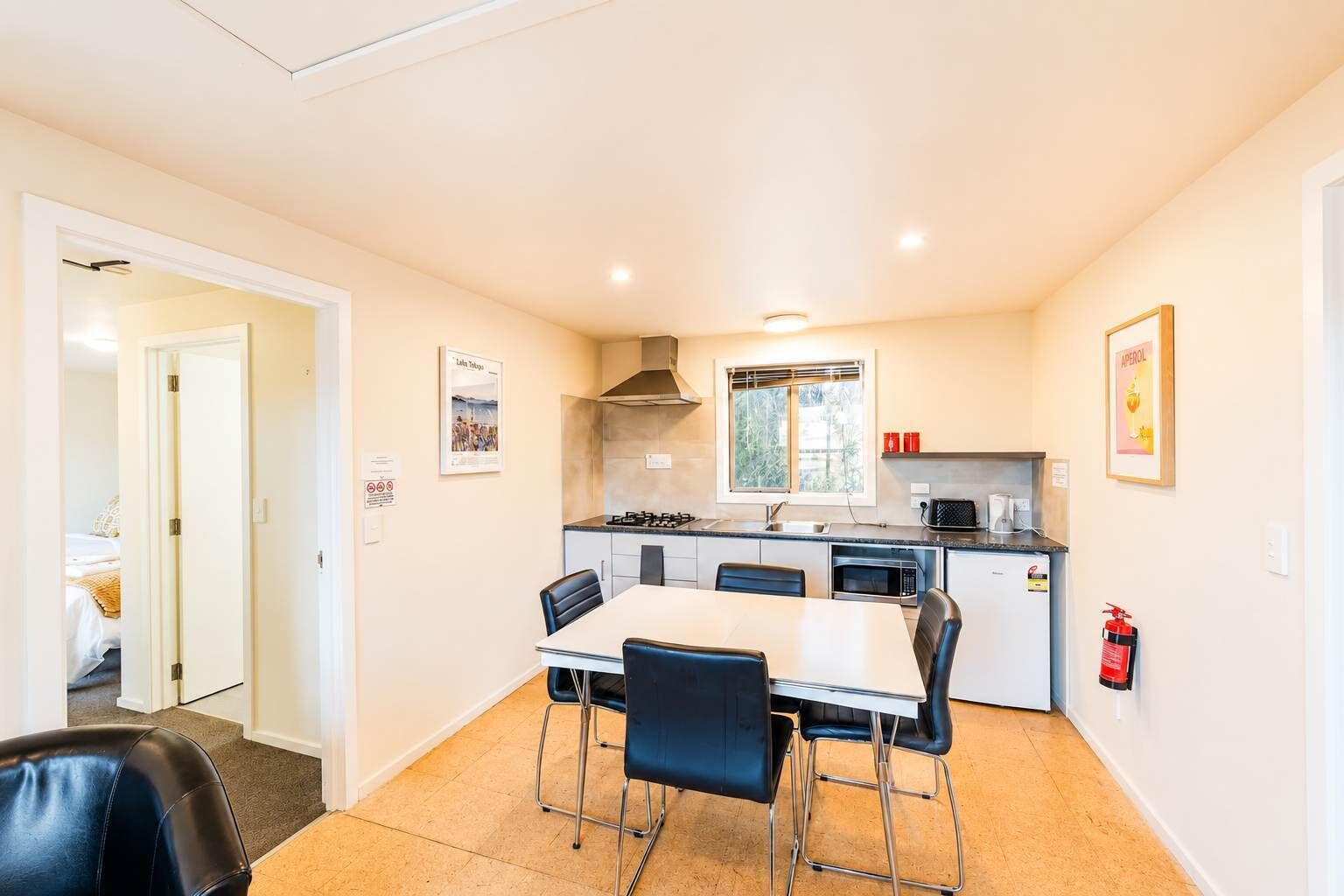 A compact kitchen with a dining area, a stove, microwave, and a fire extinguisher.