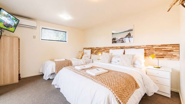 A hotel room with two beds, a television, a window, a wooden headboard, and a wall-mounted artwork. - Orion | Lake Tekapo | Hot Tub | Sleeps 3 (Lake Tekapo)